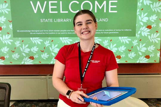 Smiling woman standing at State Library reception with an iPad.