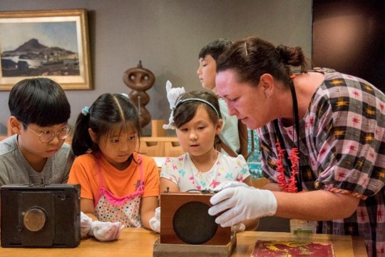 One adult and 3 children wearing white gloves and looking at vintage cameras.