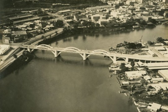Aerial photo of the bridge taken soon after the opening, showing detail of the cityscape and roads on north and south sides of the river.