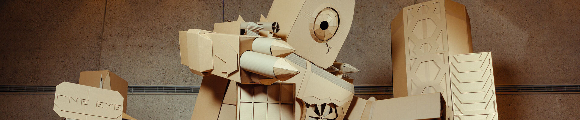Giant cardboard robot sculpture holding on to cardboard buildings and standing on a cardboard vehicle