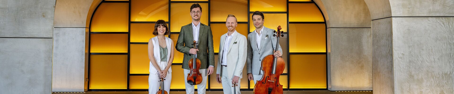 Four musicians standing in an archway holding string instruments
