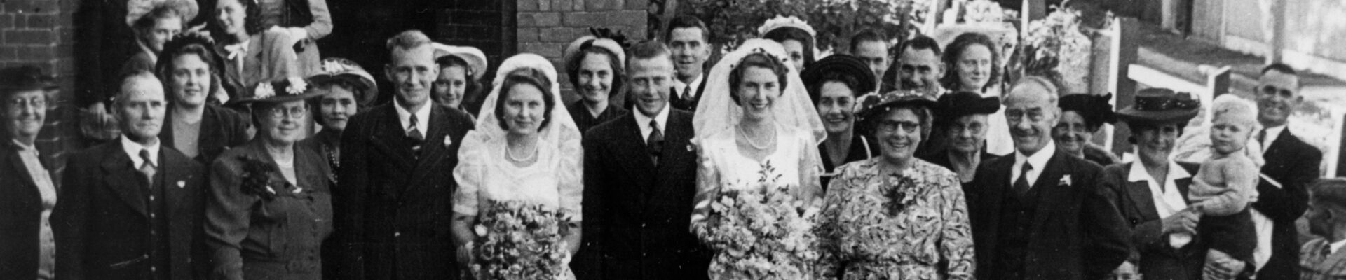 Double wedding in East Brisbane 1949 Two brides with large bouquets stand next to their grooms in front of a large group of people oustide a church