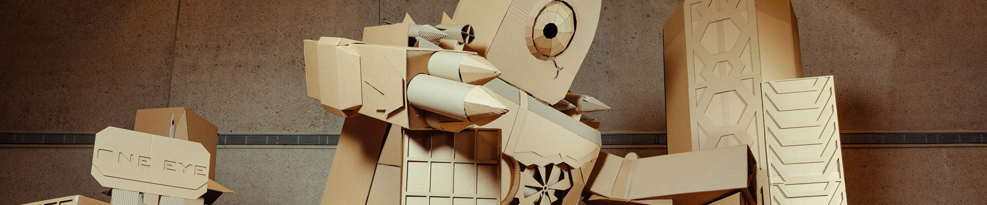 Giant cardboard robot sculpture holding on to cardboard buildings and standing on a cardboard vehicle
