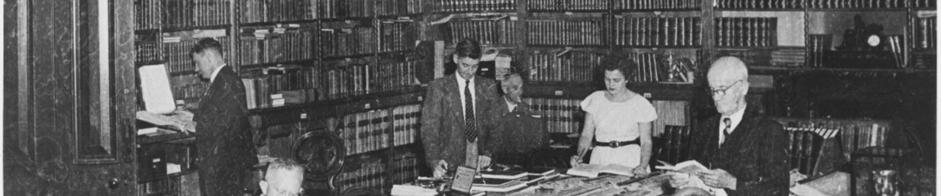 Black white photograph of seven individuals working in a library