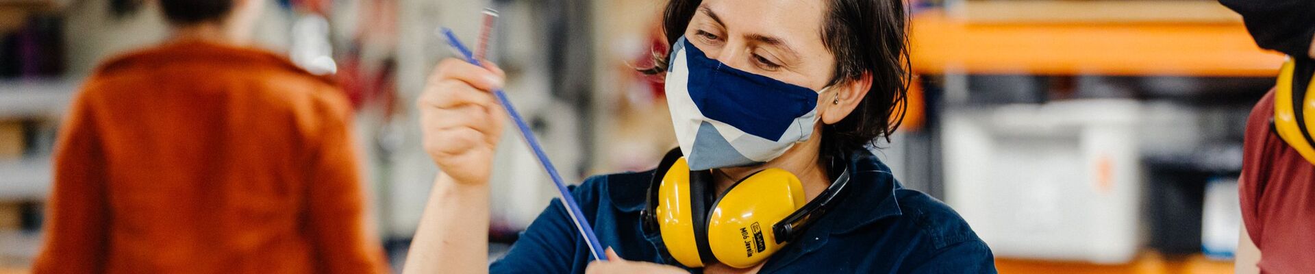 A person wearing a safety mask and muffs inspecting a blue wire