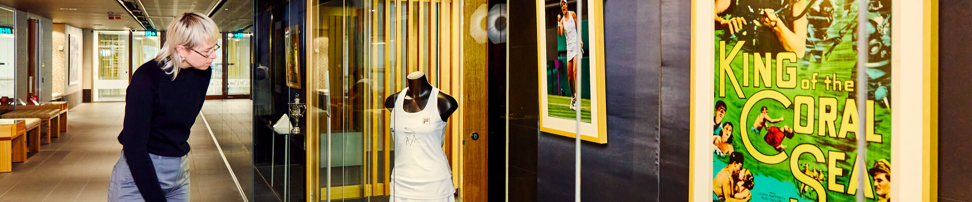 A woman with blond hair leans down to inspect a mannequin wearing Ash Bartys Wimbledon uniform