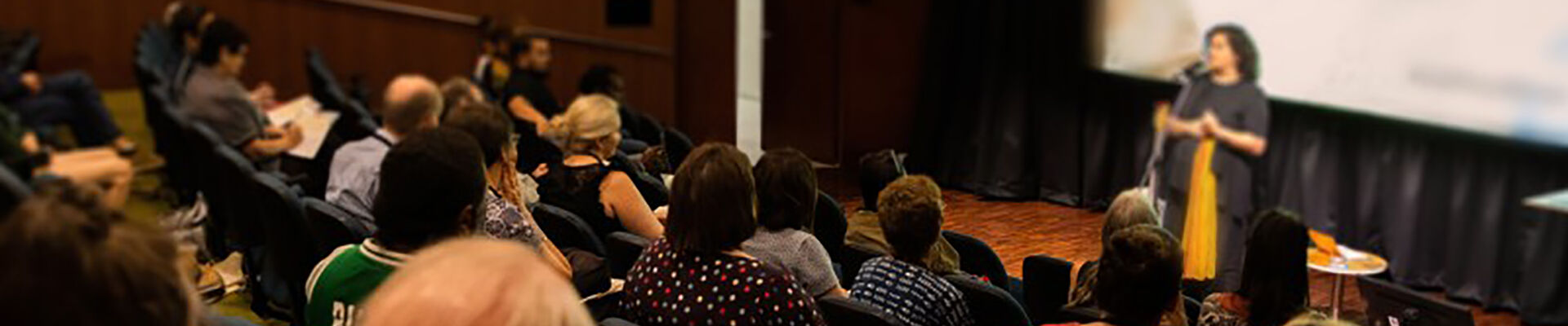 People sitting in auditorium chairs listening to speaker State Library