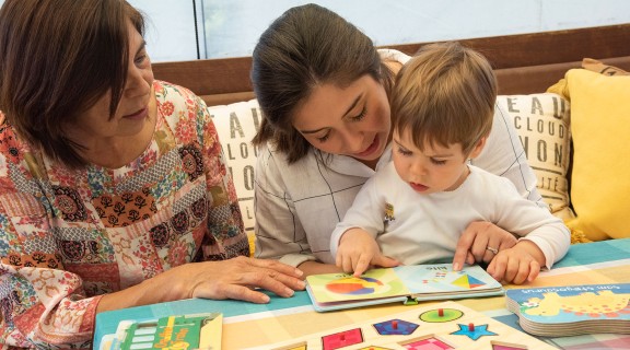 Child learning with two women through reading a book.