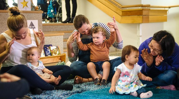 Children playing hand action games with parents in a library