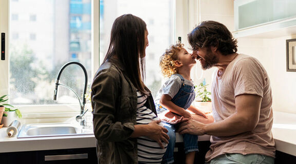 Pregnant mum, dad and preschooler having family time in kitchen