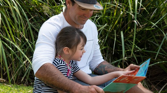Man reading a book to a girl in an outside area