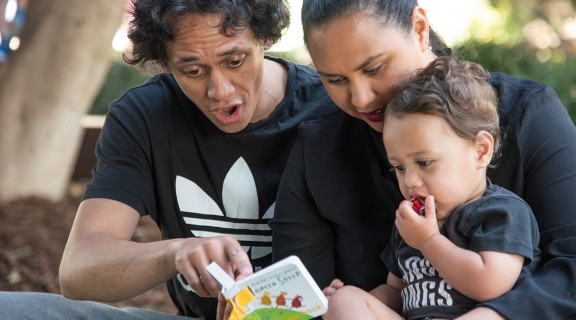 Man and woman reading a book to a child in an exciting manner