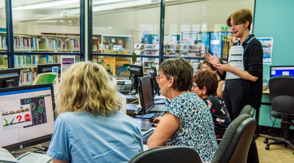 An instructor helps a group of people using laptops in a classroom.