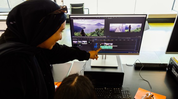 Two people looking at Premiere Pro, and editing some video content,on a deskstop computer at The Edge.