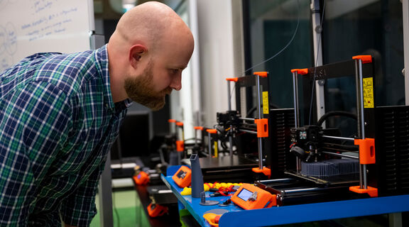 Man looking at 3D printer that is printing a model