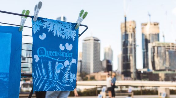 A cyanotype artwork hangs drying with the Brisbane city scape in the background