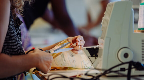 photo of a person using an overlocker at The Edge. The person is cutting a piece of fabric with scissors.