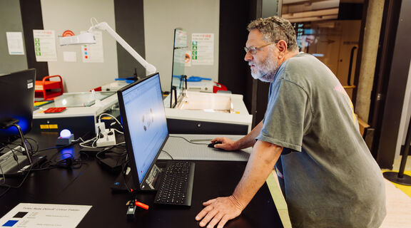 A photo of a man using a computer and laser cutter