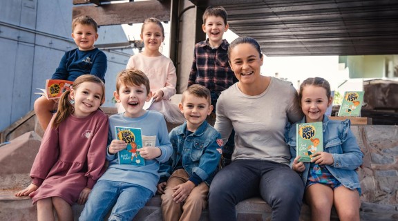 Ash Barty, Australian tennis player, sitting with a group of children holding books.