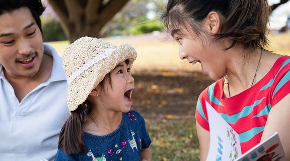 Family reading a book in the park. Little girl has mouth open in an expression of joy!