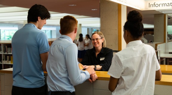 Students being helped by a smiling librarian