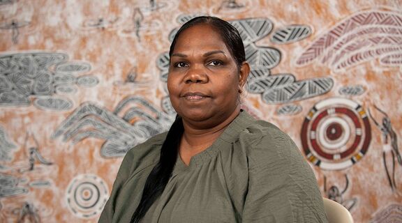 Portrait of Colleen Sam in front of her artwork Ngundurra Dreaming, 2025, photo by State Library of Queensland.