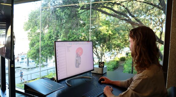 a man sitting at a computer looking at a monotor where Autodesk Fusion360 is on screen. There is a model on screen and the man is moving the mouse around to look at it