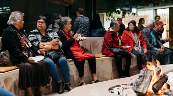 Visitors chatting and eating while gathered around a lit fire in the Talking Circle.