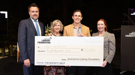 Four people smiling and holding a large presentation cheque