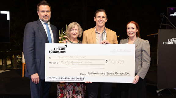 Four people smiling and holding a large presentation cheque