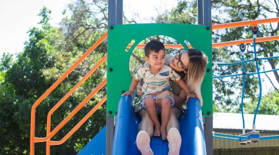 Parent and child sitting on a slide at the park