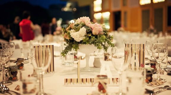 Wedding dinner setup on a round table with a flower vase centerpiece.