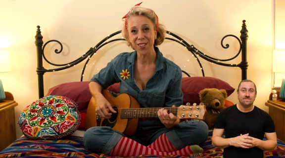 Singer Nadia Sunde sitting on a bed with a guitar