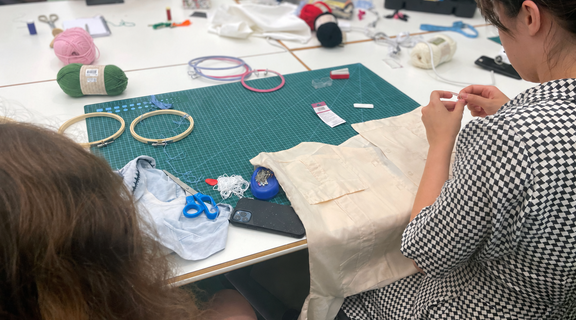 People sit around a table with embroidery hoops