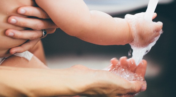 Two hands are under a running tap - a baby hand and an adult hand.