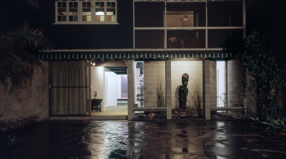 Photo of the Johnstone Gallery and courtyard. It is nighttime and it has just rained, the light from inside the gallery shines off of the wet concrete outside. 