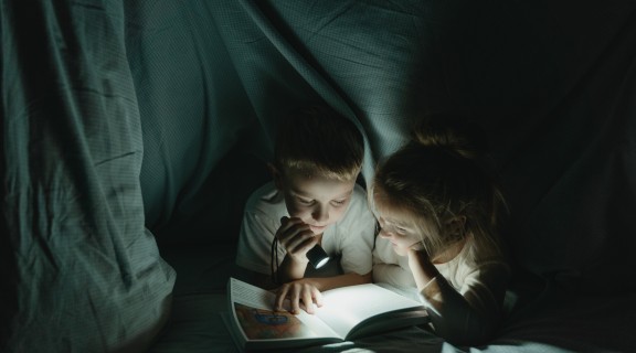 Brother and sister looking at book in torch light