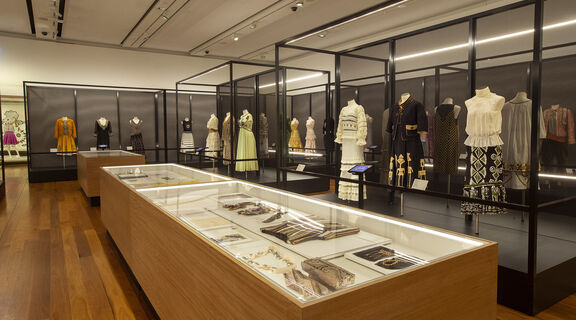 A photo inside a museum of clothes on mannequins and display boxes containing accessories