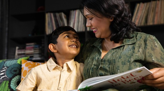 Child smiling at mother who is reading him a story