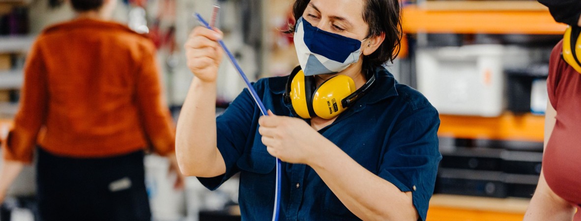 A person wearing a safety mask and muffs inspecting a blue wire