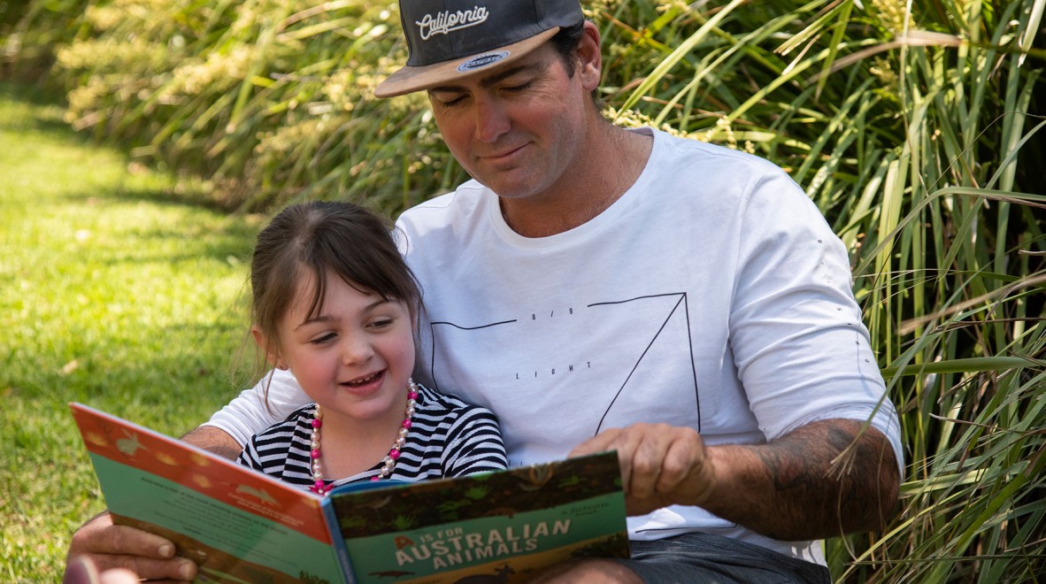 Man reading a book to a child in an outdoor area.