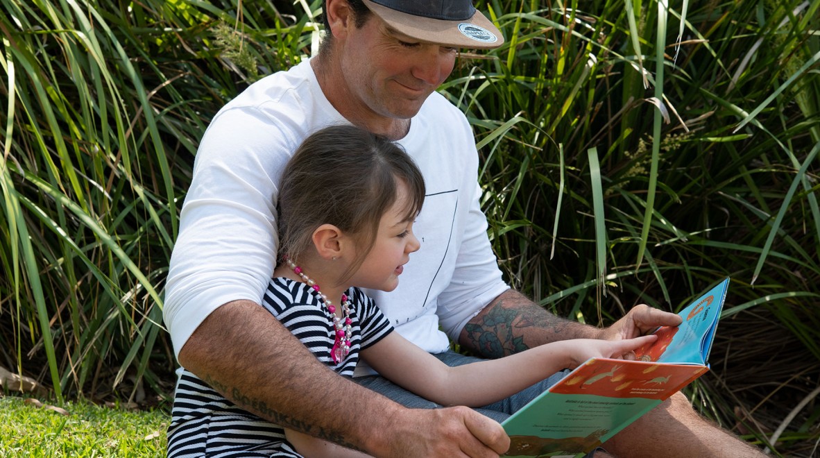 Man reading a book to a child in on the grass