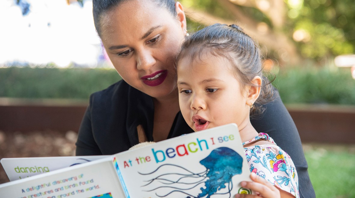 Woman reading a book to a child in an outdoor area