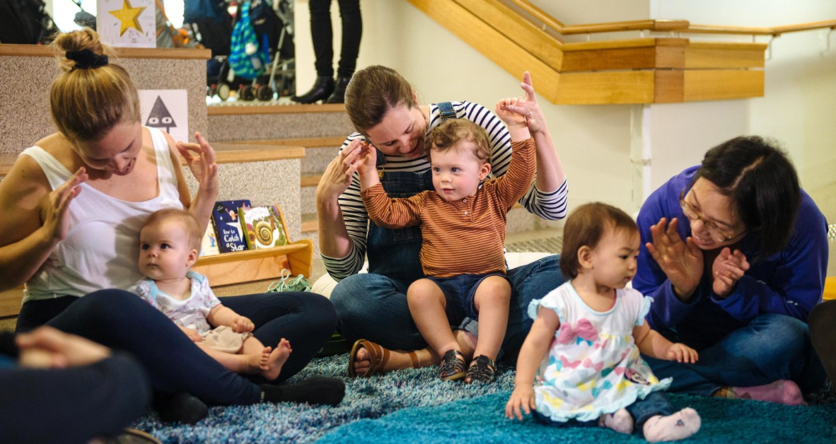 Children playing hand action games with parents in a library