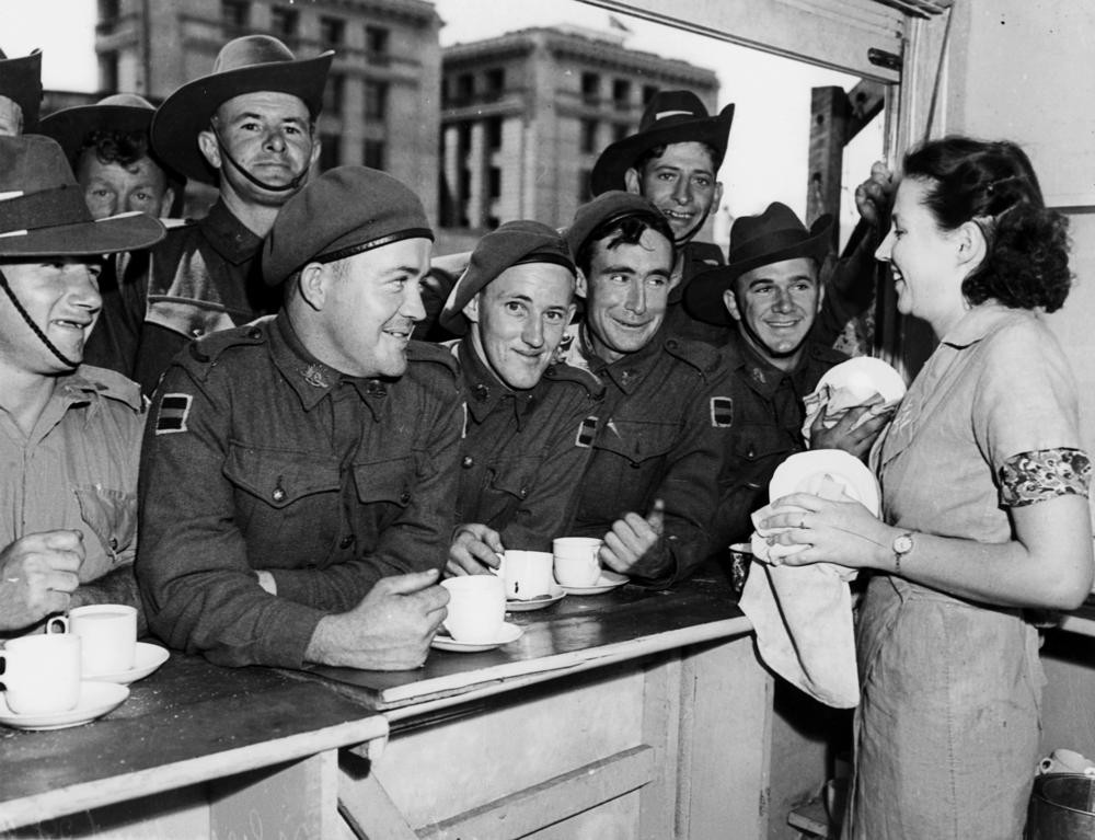 Several Soldiers enjoying a cup of tea leaning on a bench at the Silver Hut Brisbane ca 1942