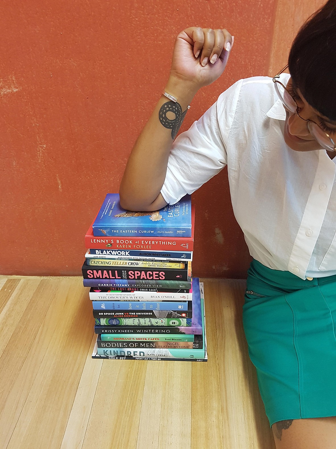 Shastra Deo sitting on a wood floor leaning her elbow against a stack of books