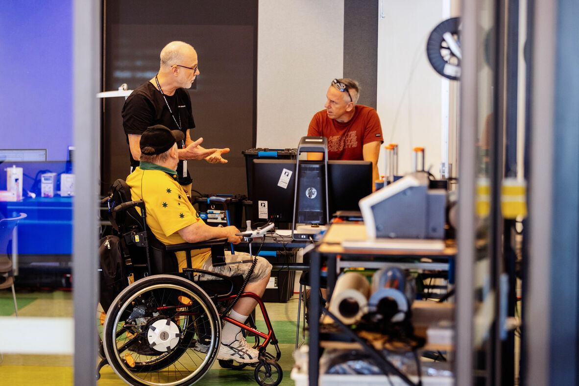 Three people talking together in a room with computers and other technology.