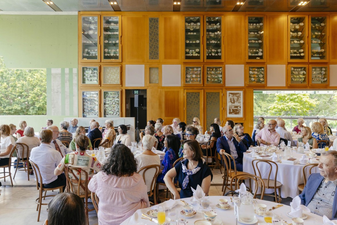 People seated around circular tables with tea cup collections displayed in cabinets in the background.
