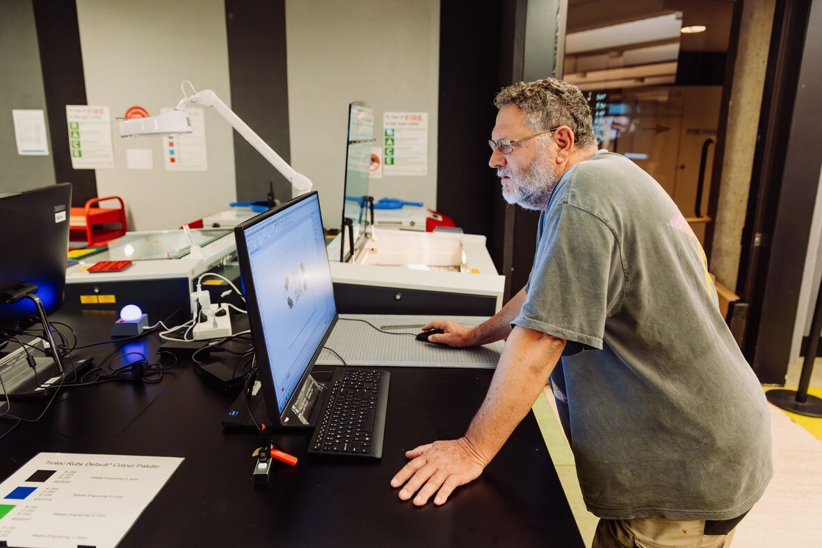 A photo of a man using a computer and laser cutter
