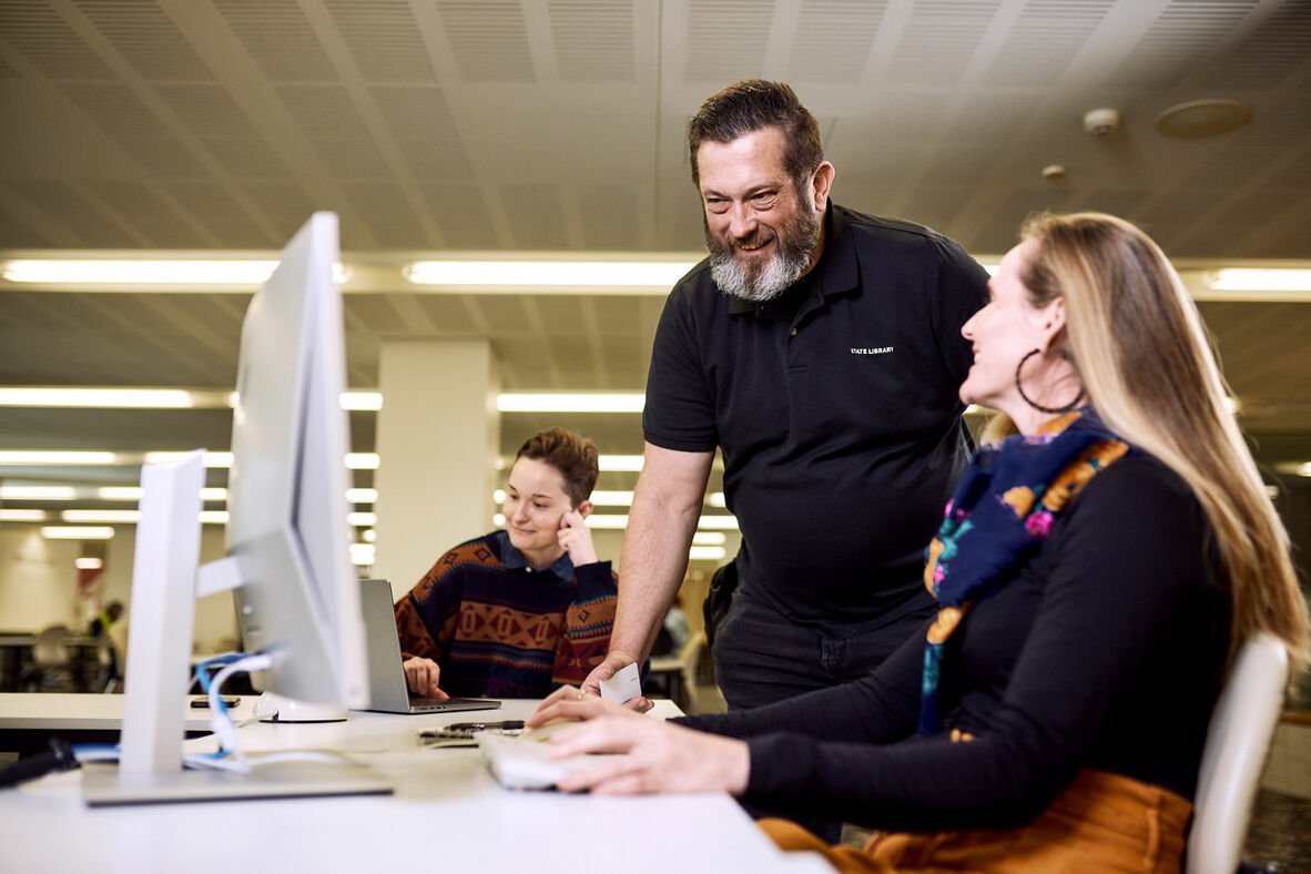State Library staff member standing beside woman using a computer.